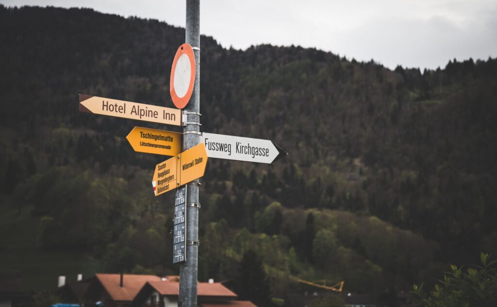 Directional signs in Sachseln, Switzerland against lush green forest backdrop.